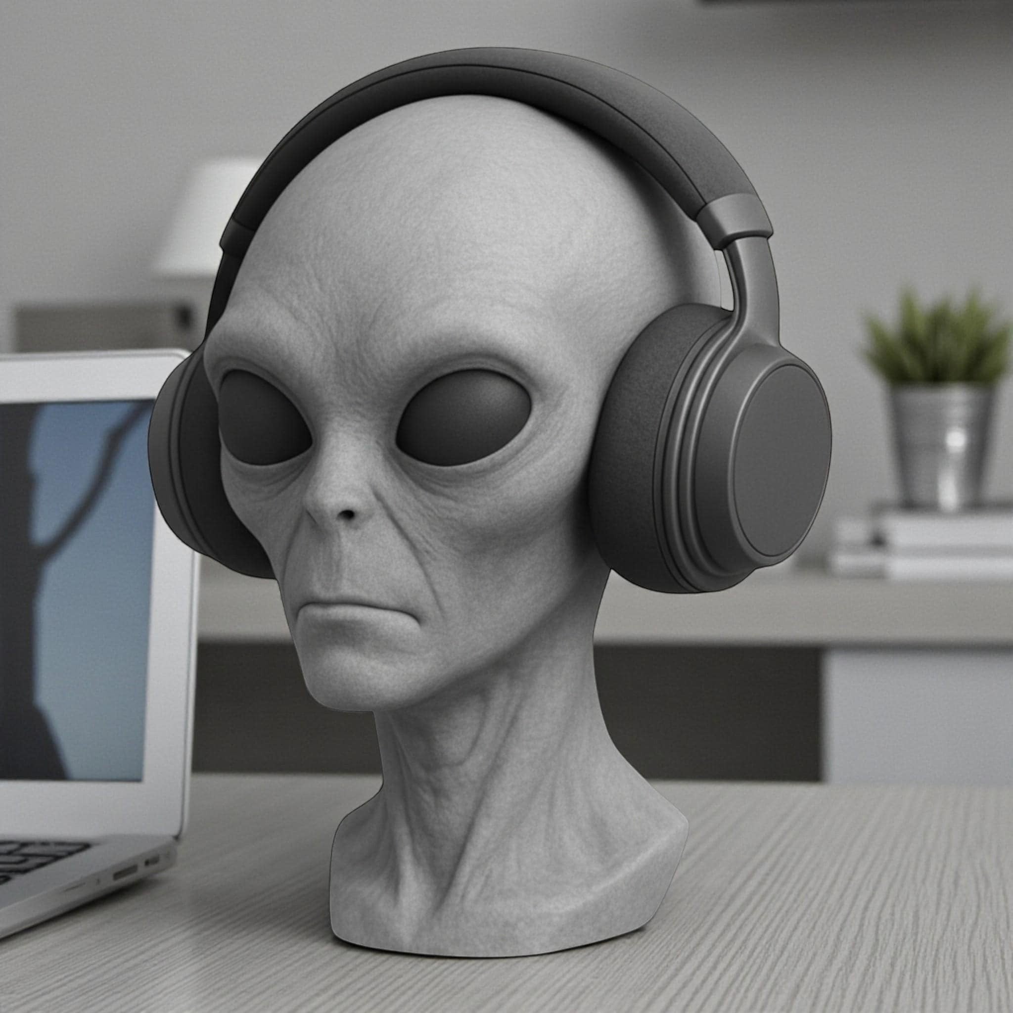 Happy3dWorld gray alien bust headphone stand holding black over-ear headphones on a desk with a laptop