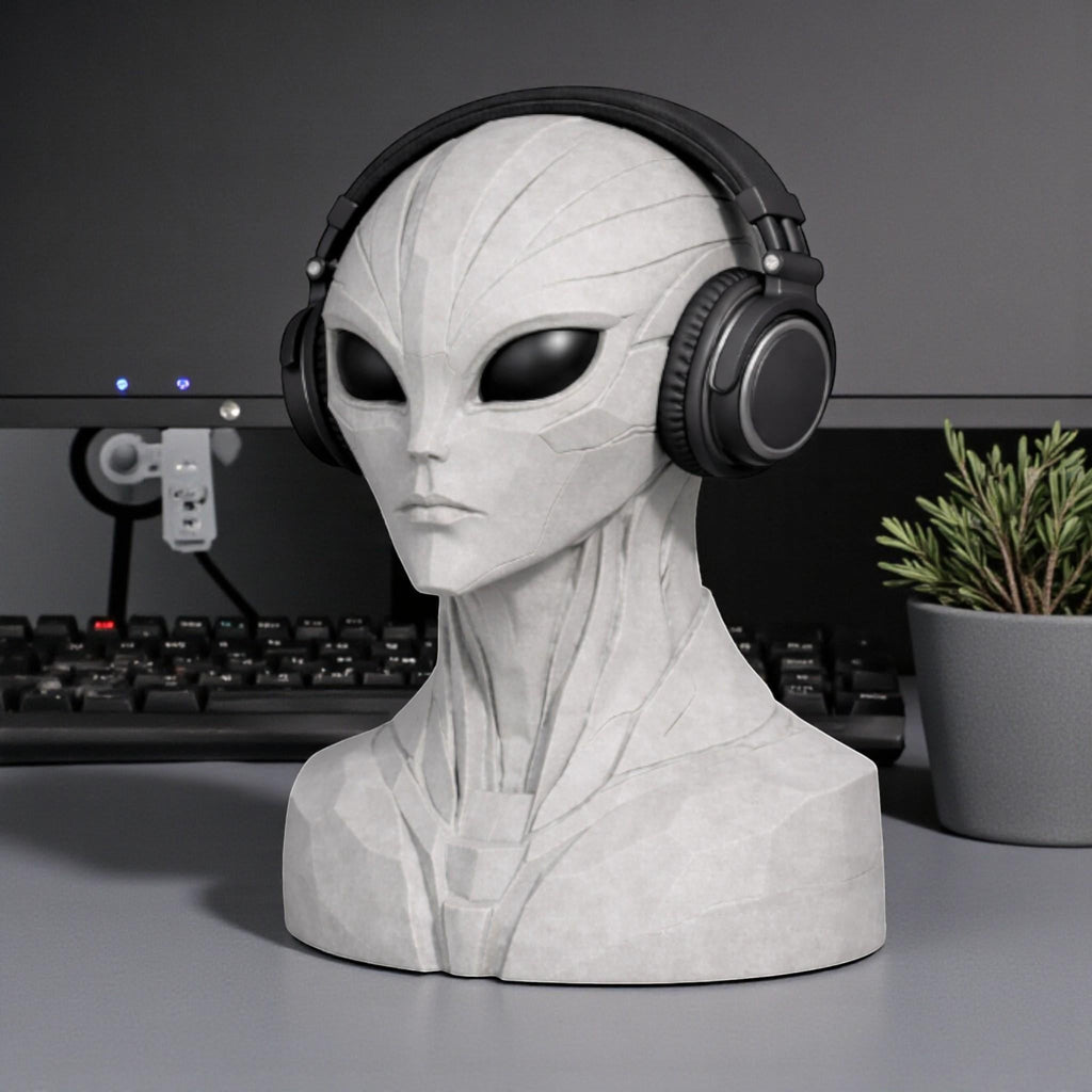 Happy3dWorld alien bust headphone stand in grey, holding black over-ear headphones on a desk with a plant.
