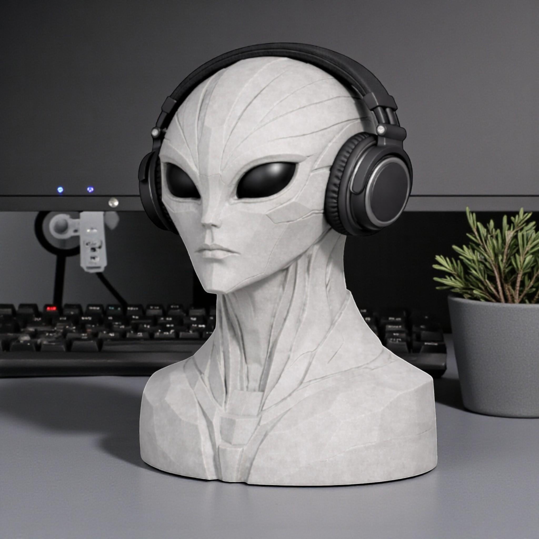 Happy3dWorld alien bust headphone stand in grey, holding black over-ear headphones on a desk with a plant.