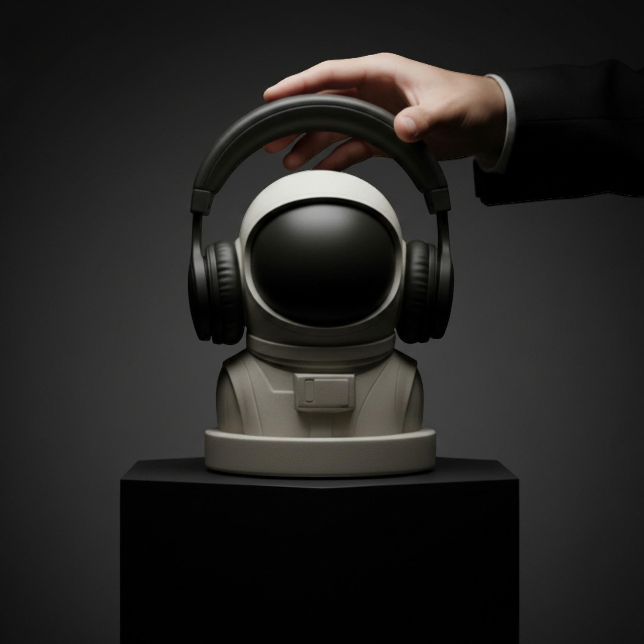 Happy3dWorld white astronaut headphone stand with black visor holding black over-ear headphones on a dark pedestal.