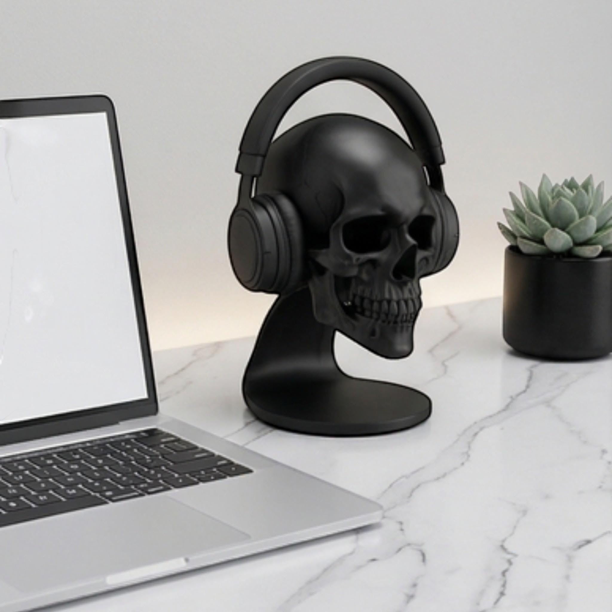 Happy3dWorld matte black anatomical skull headset stand holding over-ear headphones on a marble desk with a laptop.