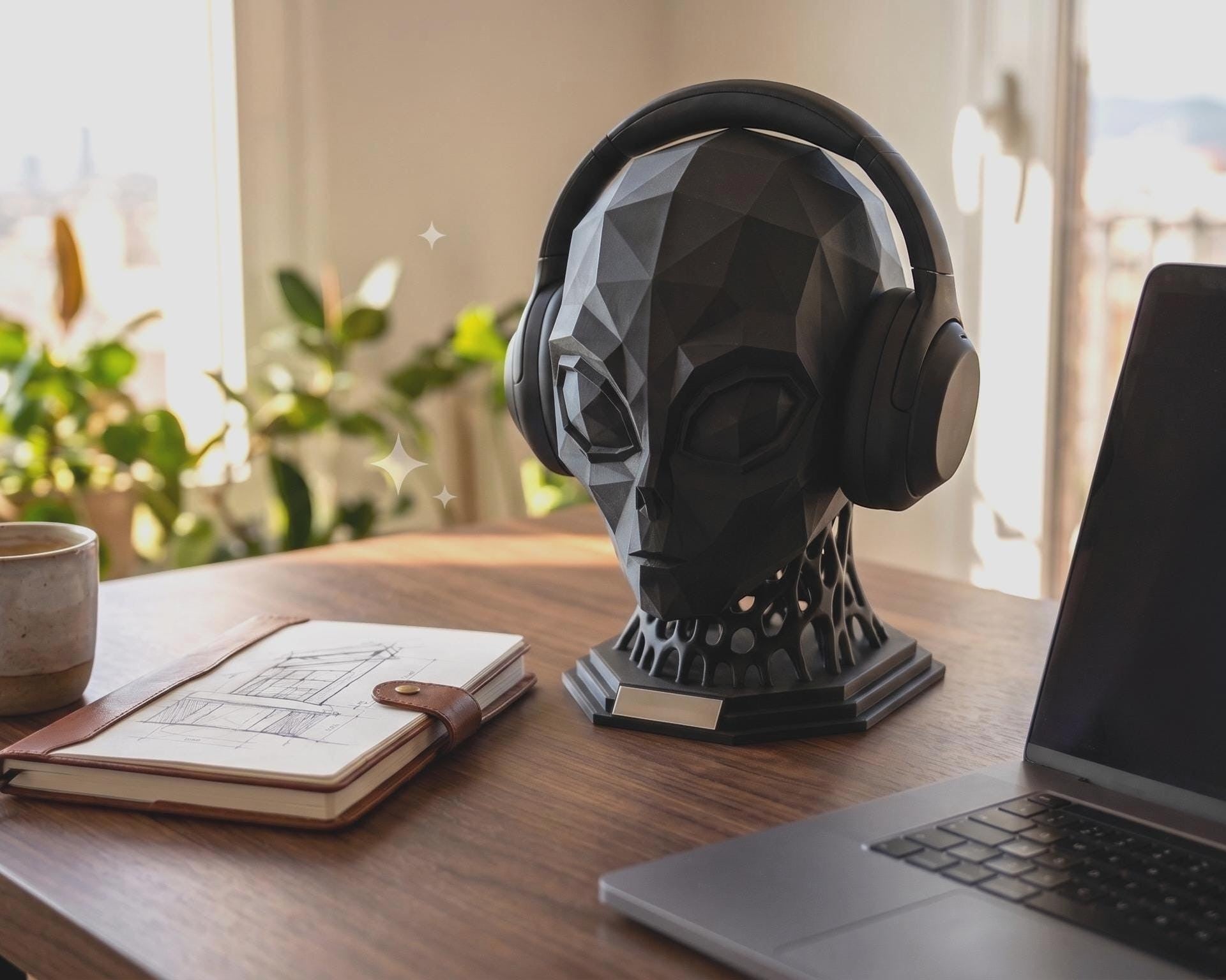 Happy3dWorld matte black low-poly alien headphone stand on a wooden desk with a laptop and notebook nearby.