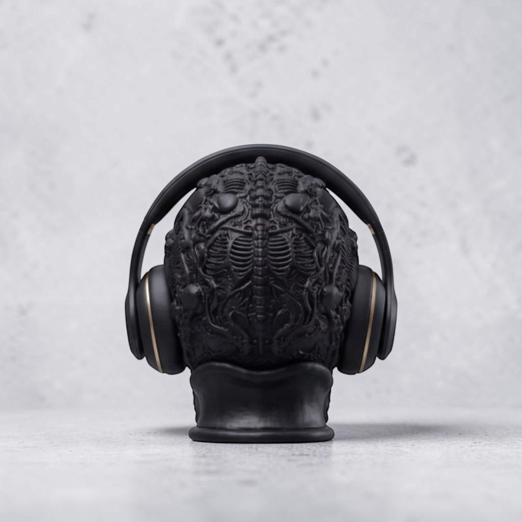 Happy3dWorld matte black gothic skull headphone stand with intricate skeletal carvings holding over-ear headphones.
