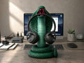 Happy3dWorld metallic green 3D printed cobra snake headphone hanger holding black over-ear headphones on a desk